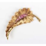 An 18ct gold and ruby brooch, designed as a leaf with a textured finish, mounted with circular cut