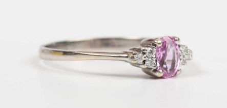 A pink sapphire and diamond ring, claw set with the oval cut pink sapphire between three circular