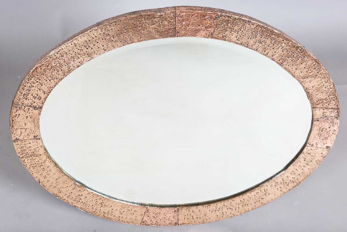 An early 20th century Arts and Crafts hammered copper oval wall mirror with riveted panels and