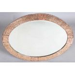 An early 20th century Arts and Crafts hammered copper oval wall mirror with riveted panels and