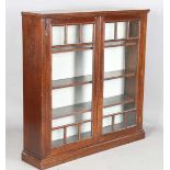 An Edwardian Arts and Crafts walnut and oak glazed bookcase, the two doors inset with curved and