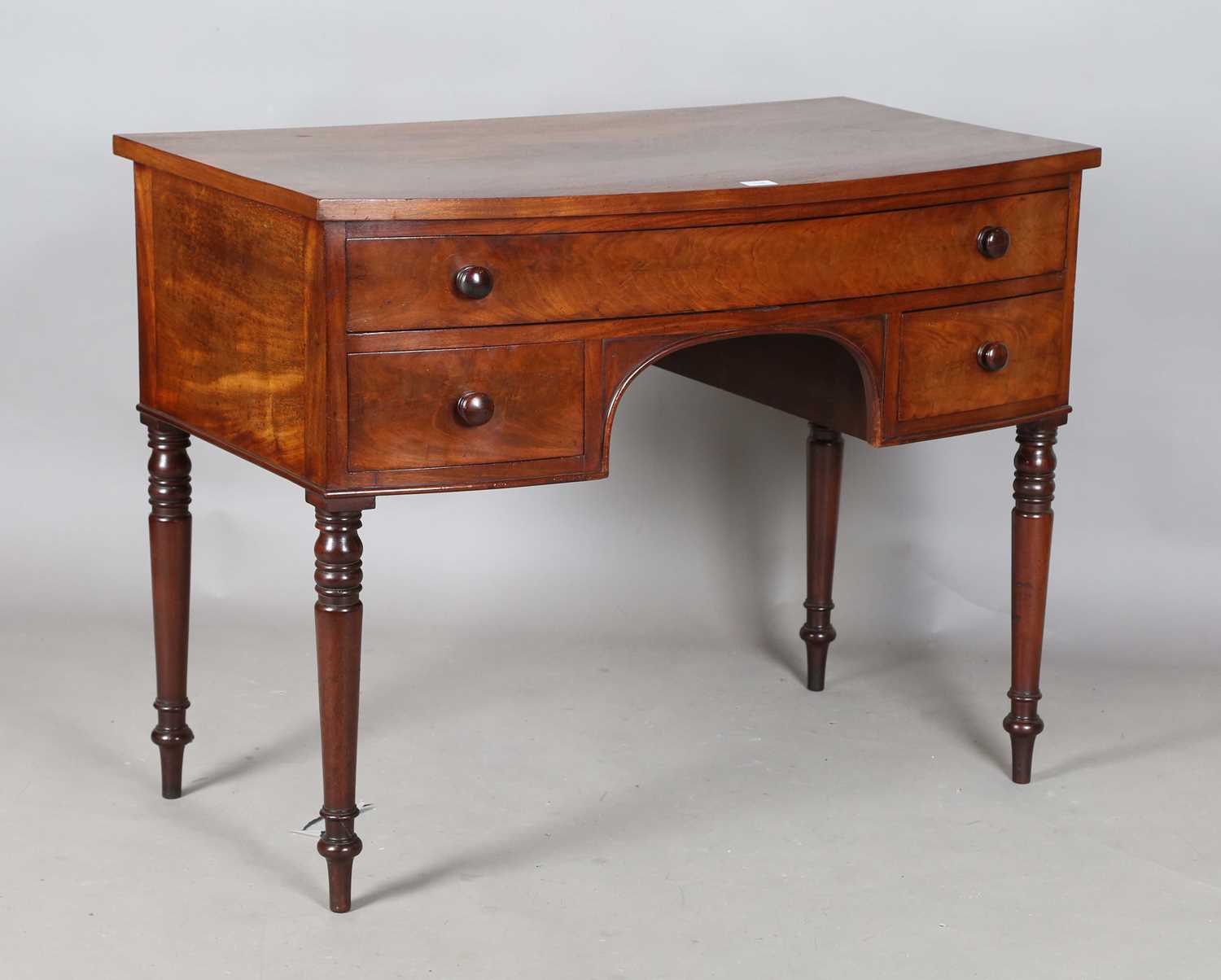 An early Victorian mahogany bowfront kneehole dressing table, fitted with three frieze drawers,
