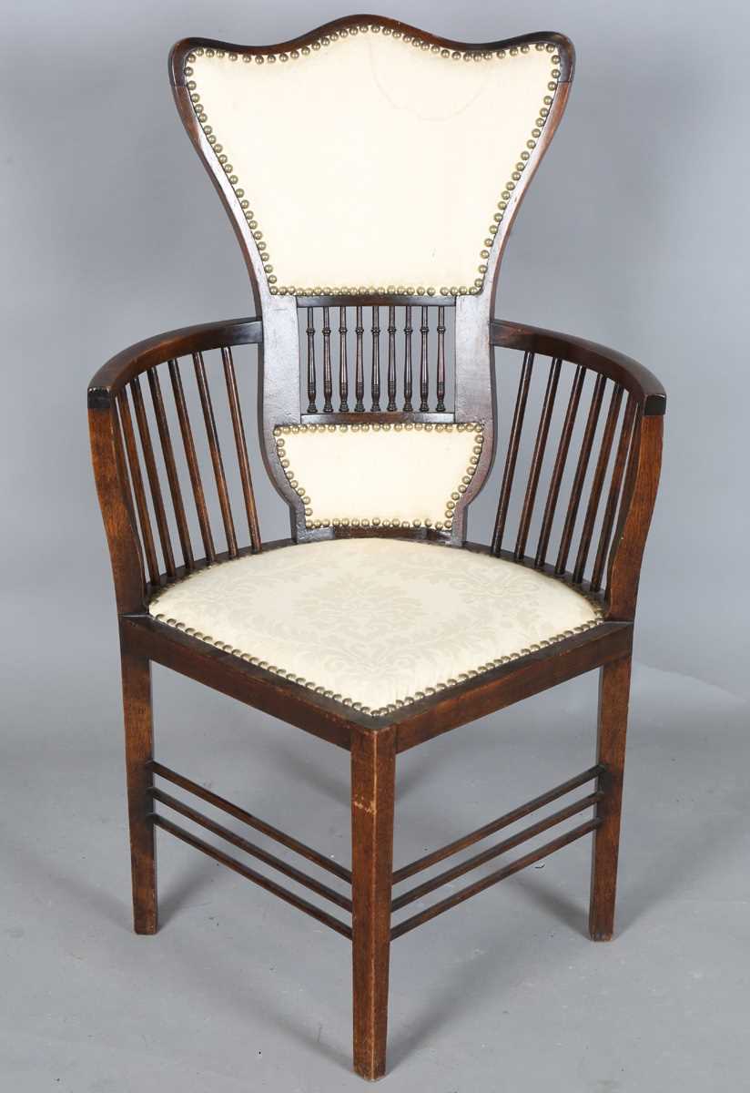 An Edwardian Arts and Crafts style stained walnut showframe armchair, upholstered in cream fabric,