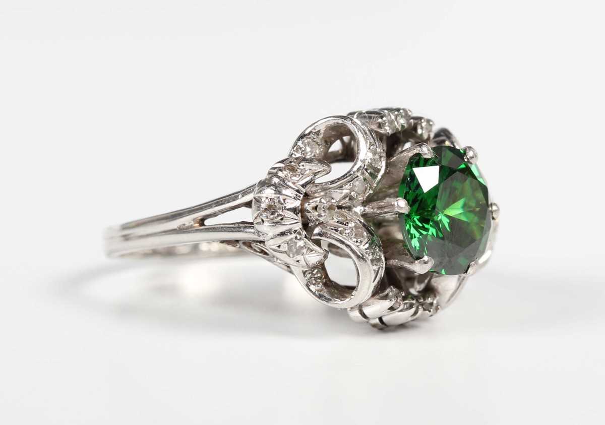 A platinum, demantoid garnet and diamond ring, claw set with the circular cut green demantoid garnet