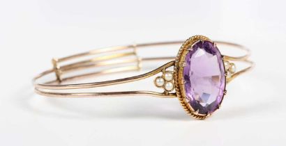 A gold, amethyst and half-pearl oval sprung bangle, claw set with the oval cut amethyst between