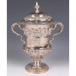 A George IV silver trophy cup and domed cover with foliate finial, the urn shaped body cast with a