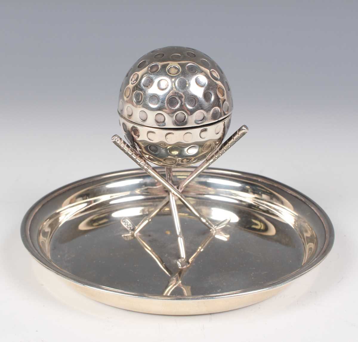 A George V silver novelty inkwell in the form of a golf ball supported by three crossed golf