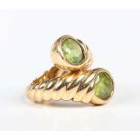 A gold and peridot two stone ring in a crossover design with ridged decoration, detailed ‘750