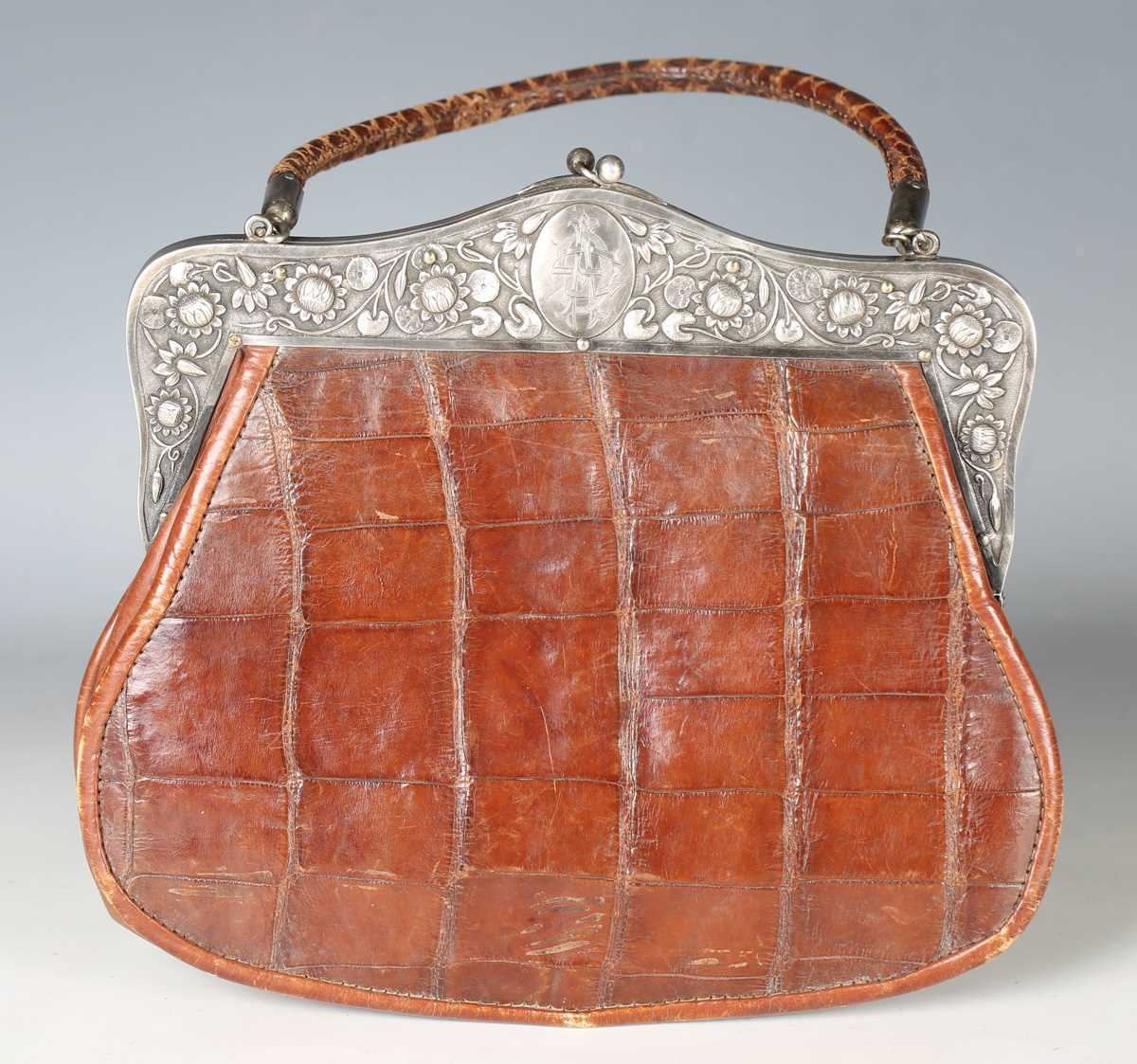 An early 20th century crocodile skin handbag, the white metal clasp decorated with lotus flowers and