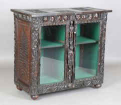 A late 19th century Continental stained oak cabinet, profusely carved with foliage, masks and