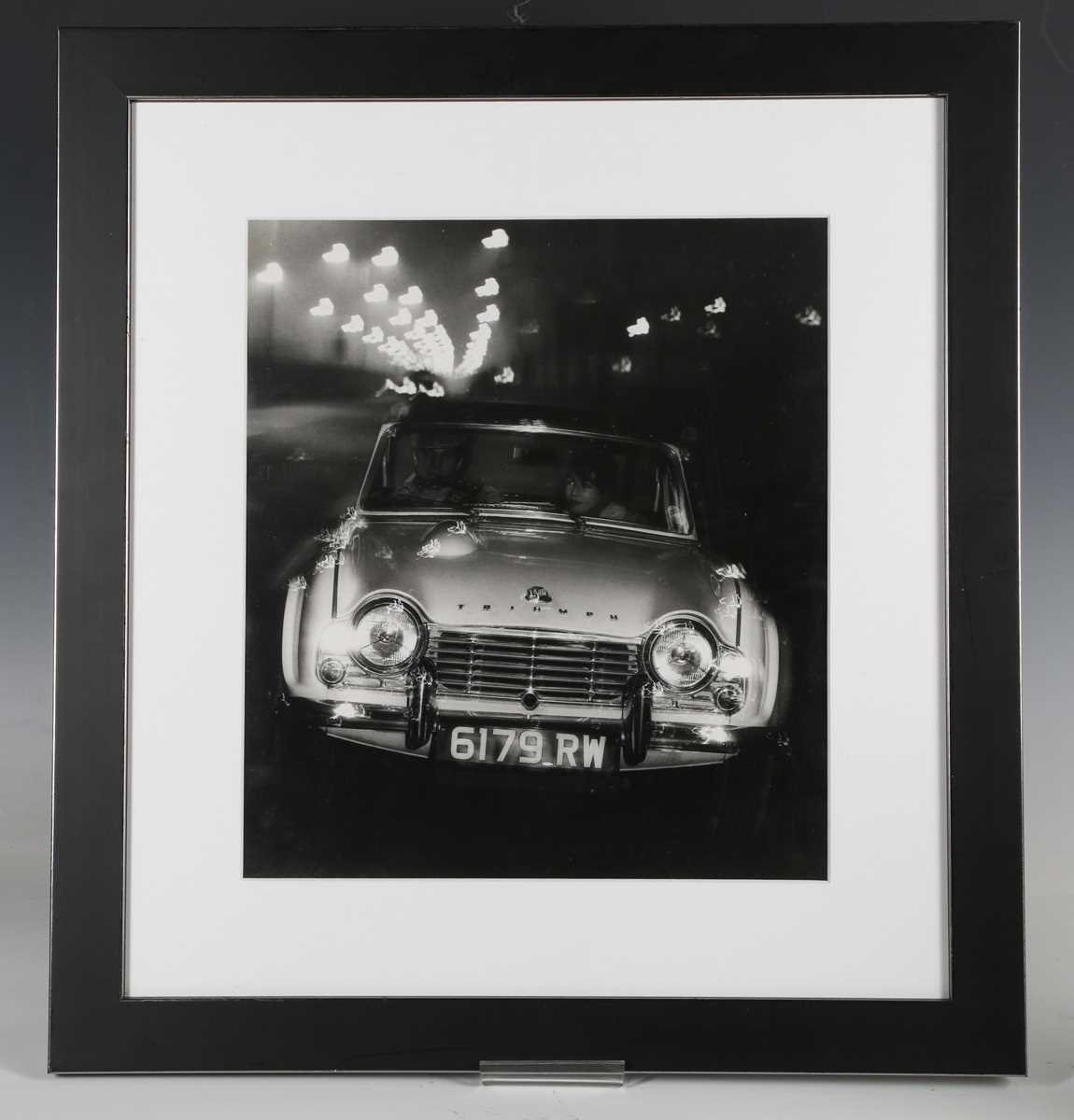 PHOTOGRAPHS. A black and white photograph of a Triumph TR4 driving along a street-lit road, 1960s or