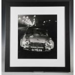 PHOTOGRAPHS. A black and white photograph of a Triumph TR4 driving along a street-lit road, 1960s or