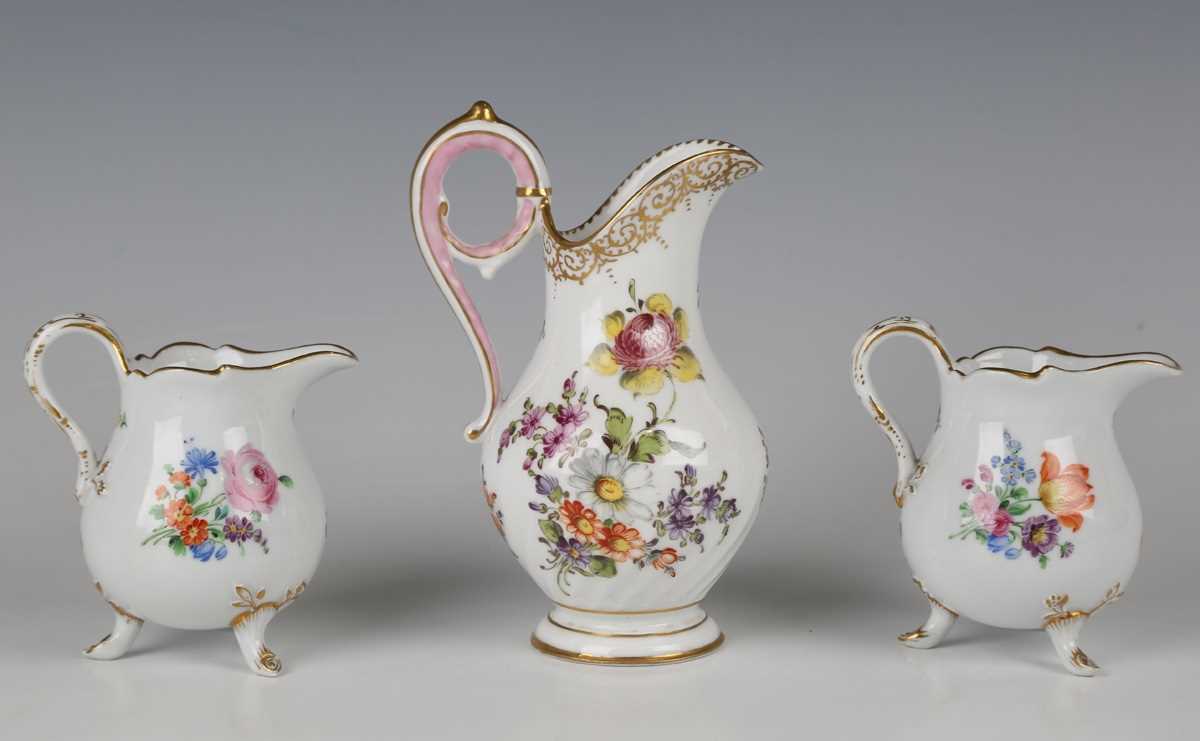 A pair of Meissen cream jugs, 20th century, painted with scattered flowers, raised on gilt