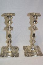 A pair of George V silver candlesticks with ornate tapered stems and square-shaped bases,