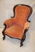 A Victorian mahogany spoon-back easy chair upholstered in buttoned fabric on scroll legs with