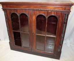 A William IV mahogany bookcase with shelves enclosed by two arched glazed doors flanked by turned