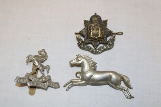 Three various military cap badges including East Surrey Regiment etc.