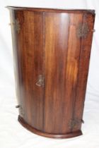 A 19th century oak curved hanging corner cupboard with shelves enclosed by two curved doors