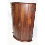 A 19th century oak curved hanging corner cupboard with shelves enclosed by two curved doors