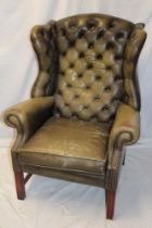 A mahogany traditional wing easy chair upholstered in green buttoned leather