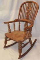 An old polished elm and beech Windsor-style rocking chair with splat and spindle back and shaped