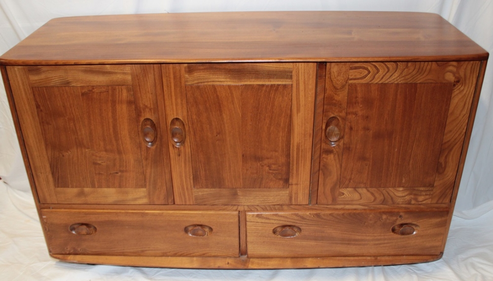 A 1960's/70's Ercol pale elm sideboard with cupboard enclosed by three panelled doors above three