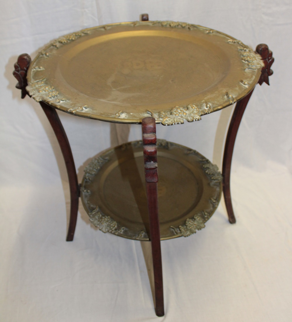 An Eastern occasional table with twin brass tray tops with decorated edges on carved wood folding