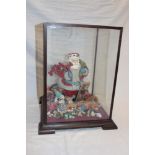 A modern Father Christmas display with other decorations within a mahogany glazed display case,