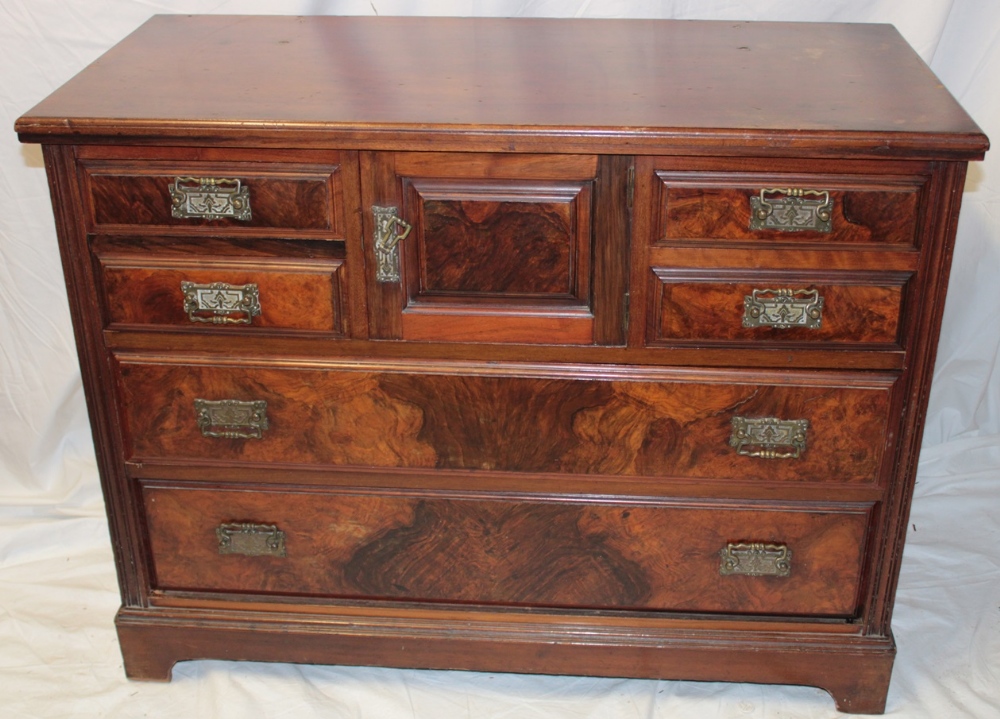 A late Victorian walnut chest with central cupboard enclosed by a small panelled door flanked by