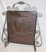 An Arts & Crafts iron fire screen with central copper panel decorated in relief with a Viking ship