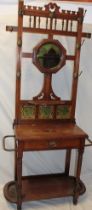 A late Victorian oak slim hall stand with circular mirror back above three ceramic tiles and a