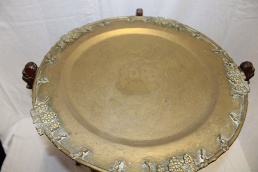 An Eastern occasional table with twin brass tray tops with decorated edges on carved wood folding - Image 2 of 2