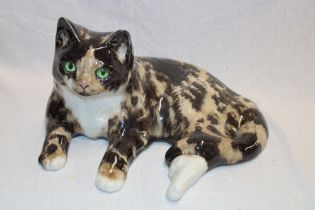 A pottery figure of a recumbent cat by Winstanley with glass eyes, 13" long,