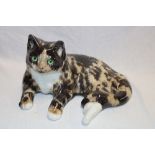 A pottery figure of a recumbent cat by Winstanley with glass eyes, 13" long,
