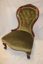 A Victorian carved mahogany easy chair upholstered in green buttoned fabric on scroll legs