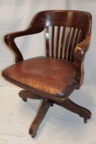 An Edwardian oak swivel office chair with rail back and leather upholstered seat