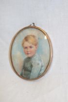 A miniature watercolour portrait depicting a bust portrait of a young boy in gilt oval locket frame