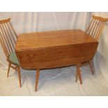 An Ercol pale elm drop-leaf dining table on square tapered legs together with a pair of