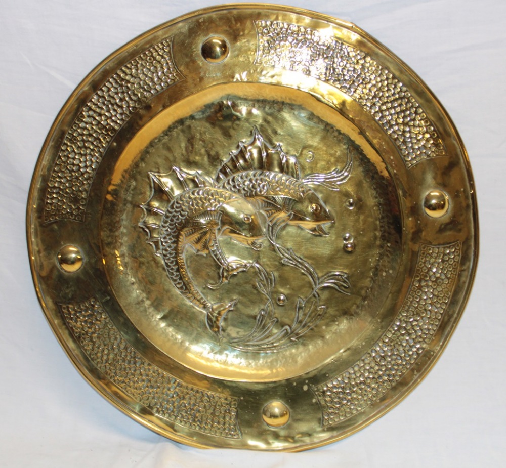 A brass circular embossed wall plaque, the centre decorated in relief with two fish,