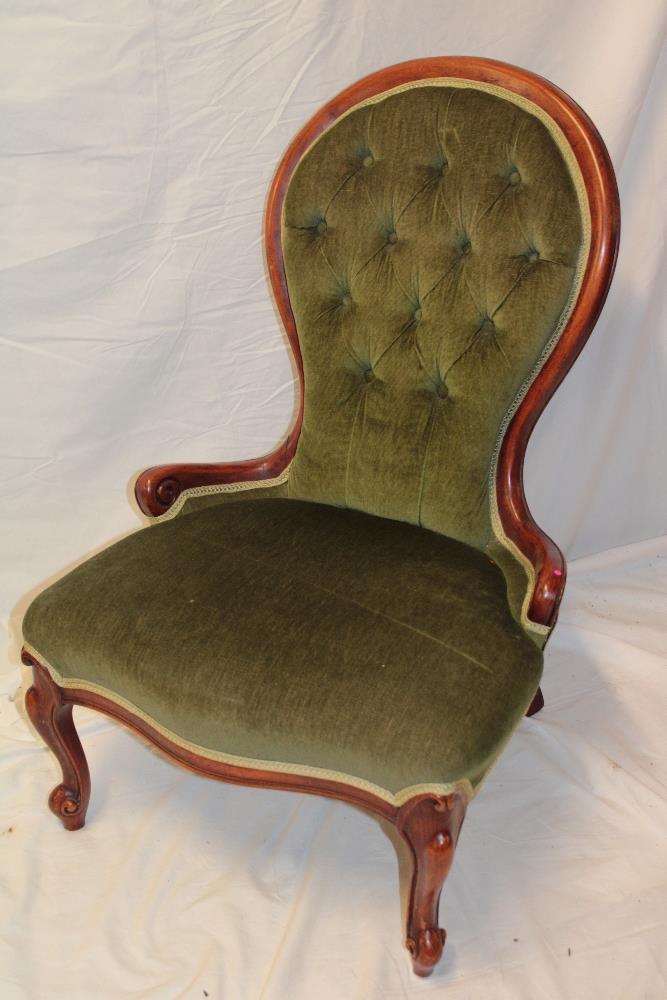 A Victorian beech spoon-back ladies' easy chair upholstered in green buttoned fabric on scroll legs