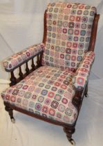 A Victorian mahogany easy chair upholstered in floral tapestry fabric on turned legs with castors