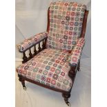 A Victorian mahogany easy chair upholstered in floral tapestry fabric on turned legs with castors