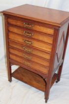 An Edwardian walnut music chest of six short drawers with folding fronts on square-shaped legs