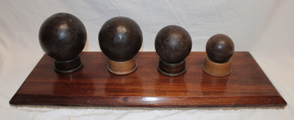 A display of four 18th and 19th century iron cannon balls, 4½" diameter - 2½" diameter,