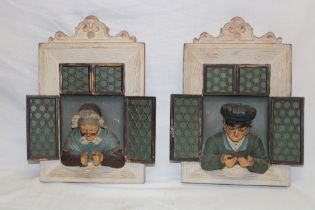 A pair of Continental pottery wall plaques depicting an elderly lady and gentleman peering from