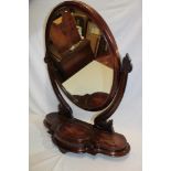 A Victorian mahogany oval swing toilet mirror on scroll-shaped supports,