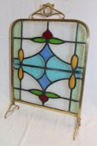 An Edwardian brass fire screen with coloured leaded glass panel on scroll shaped legs