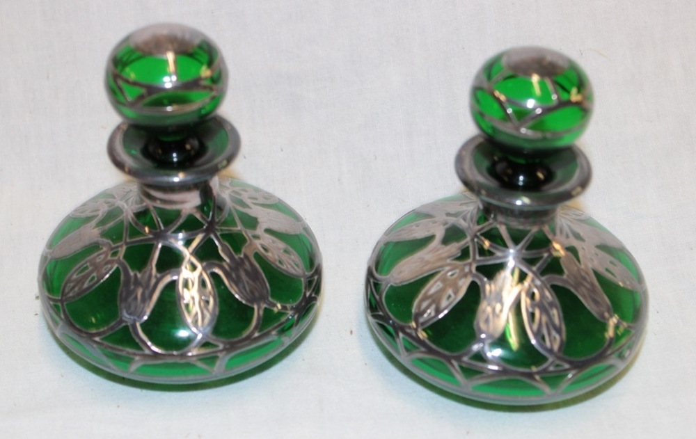 A pair of American green-tinted glass squat-shaped scent bottles with silver overlaid decoration,