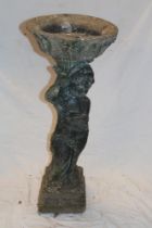 A weathered composition garden bird bath with cherub decorated stem on square base,