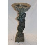 A weathered composition garden bird bath with cherub decorated stem on square base,